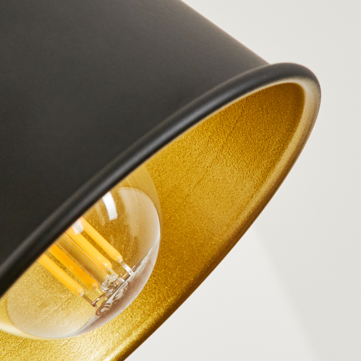 Nahaufnahme einer schwarzen Lampe mit goldenem Innenleben und sichtbarer Glühbirne.
