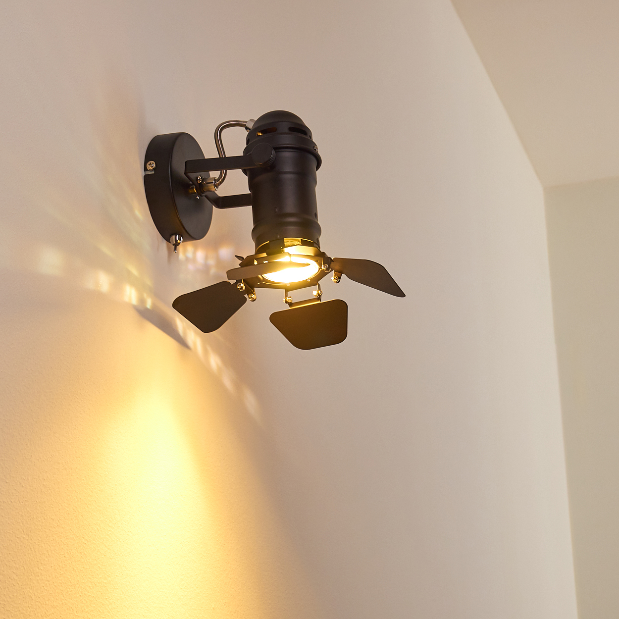 Schwarzer Wandstrahler mit verstellbaren Flügeln und warmem Lichtschein.