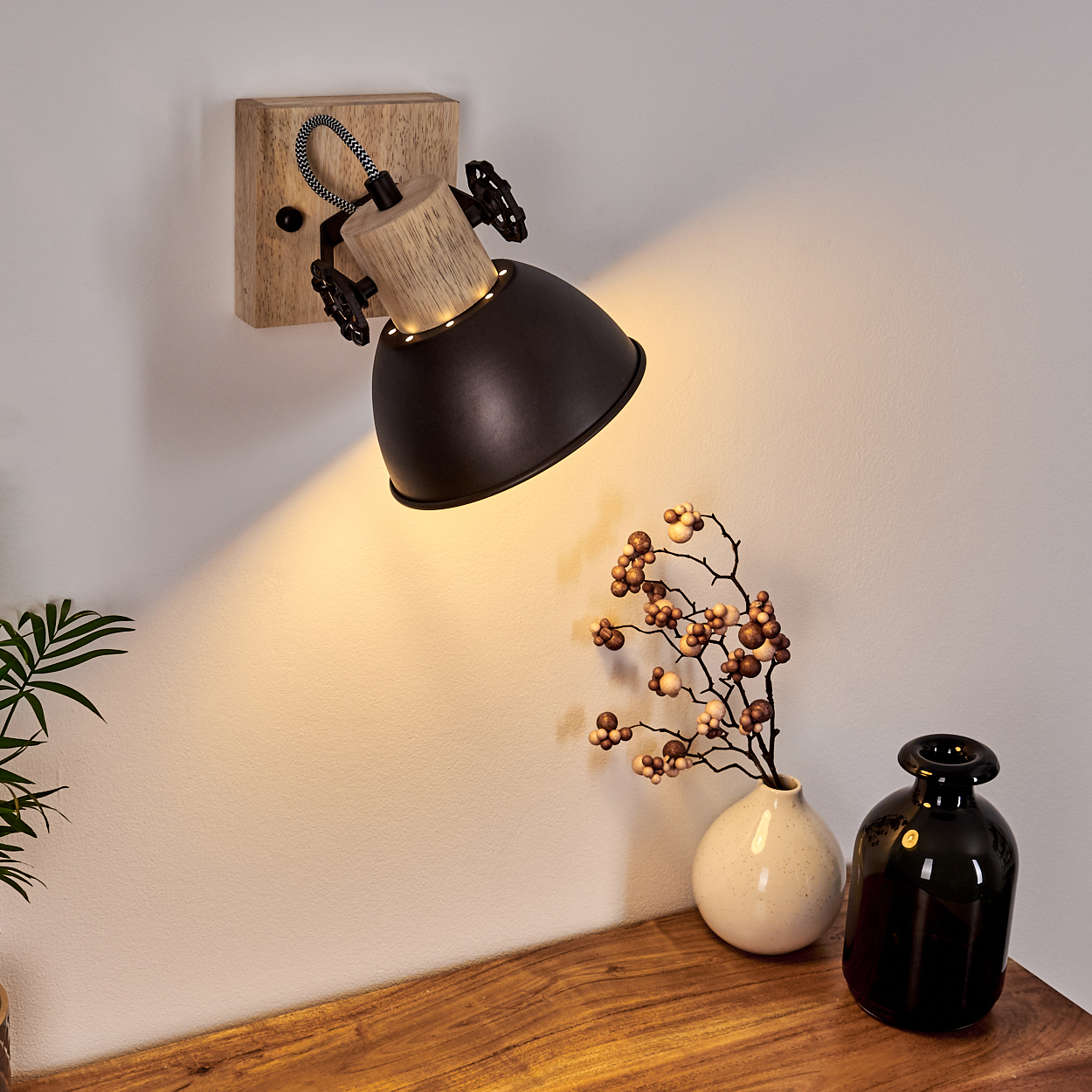 Ein schwarzer Wandstrahler mit Holzdetails leuchtet auf eine weiße Wand.