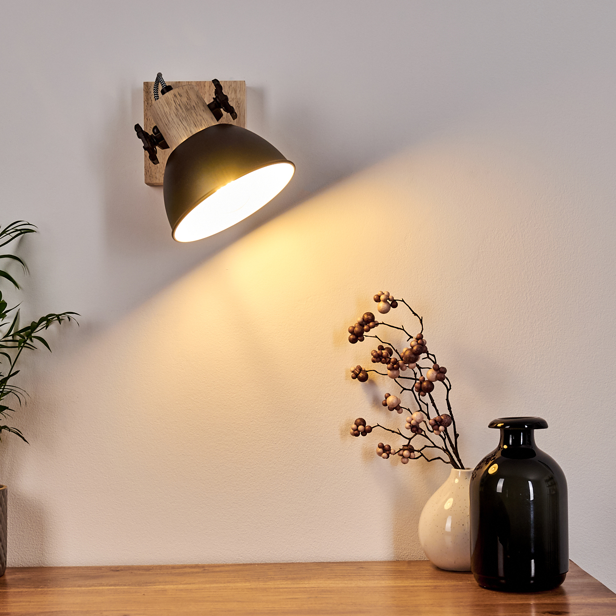 Ein Wandstrahler beleuchtet eine Wand mit zwei Vasen und Zweigen.