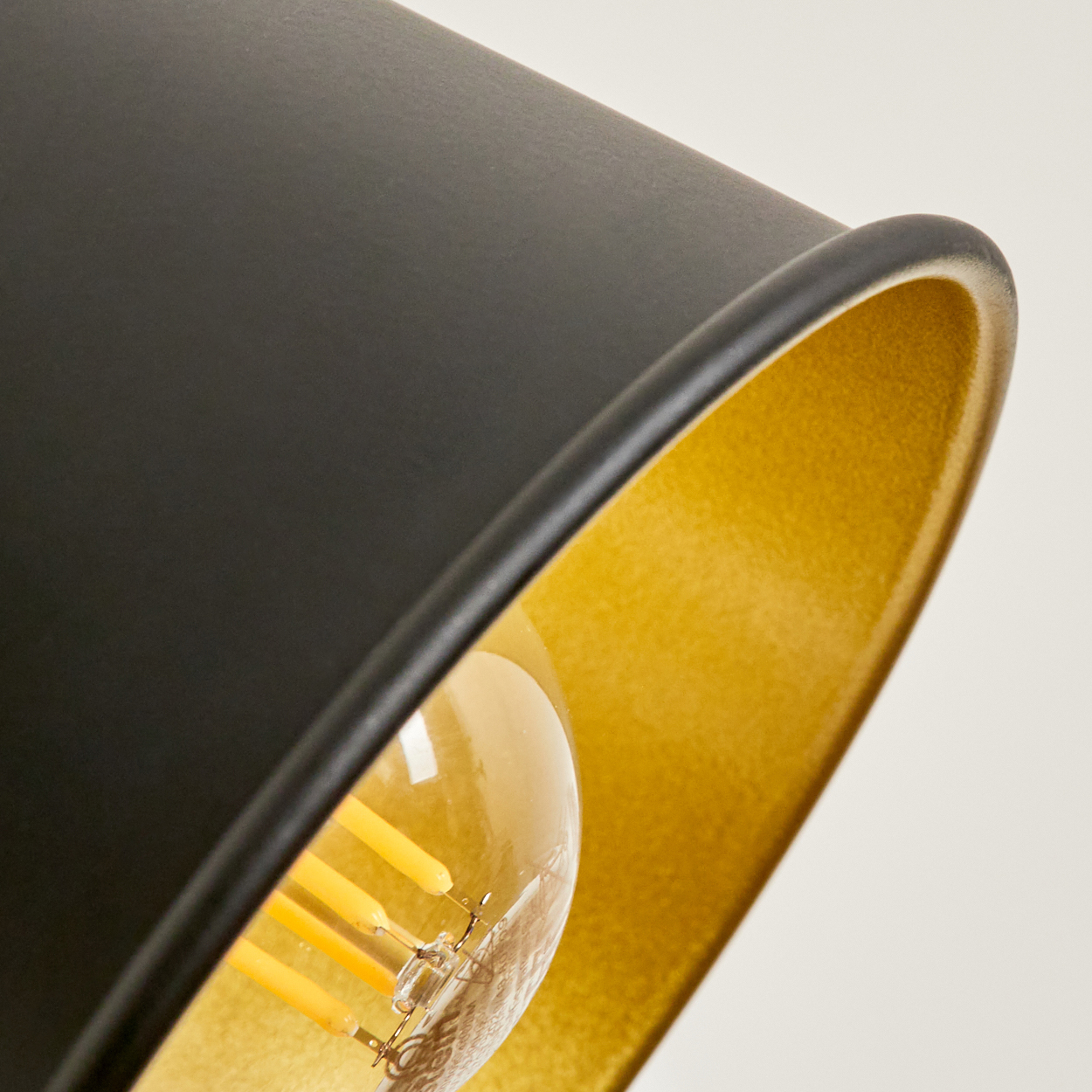 Nahaufnahme einer schwarzen Lampe mit goldener Innenseite und Glühbirne.