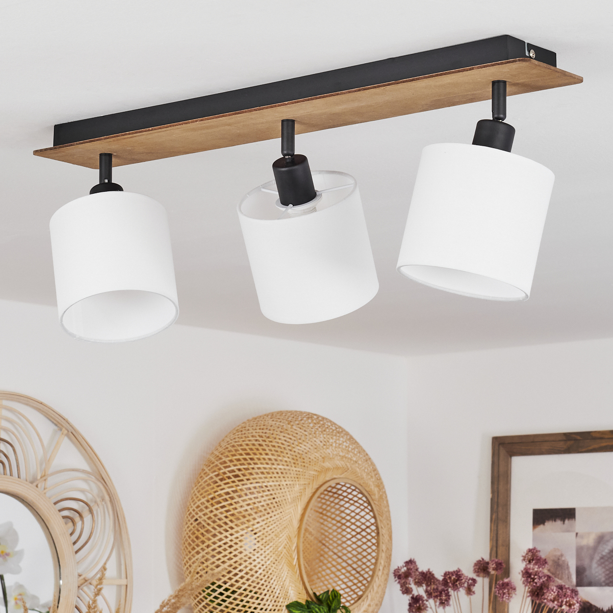 Eine moderne Deckenleuchte mit drei weißen zylindrischen Schirmen und einem Holz-Schwarz-Sockel.