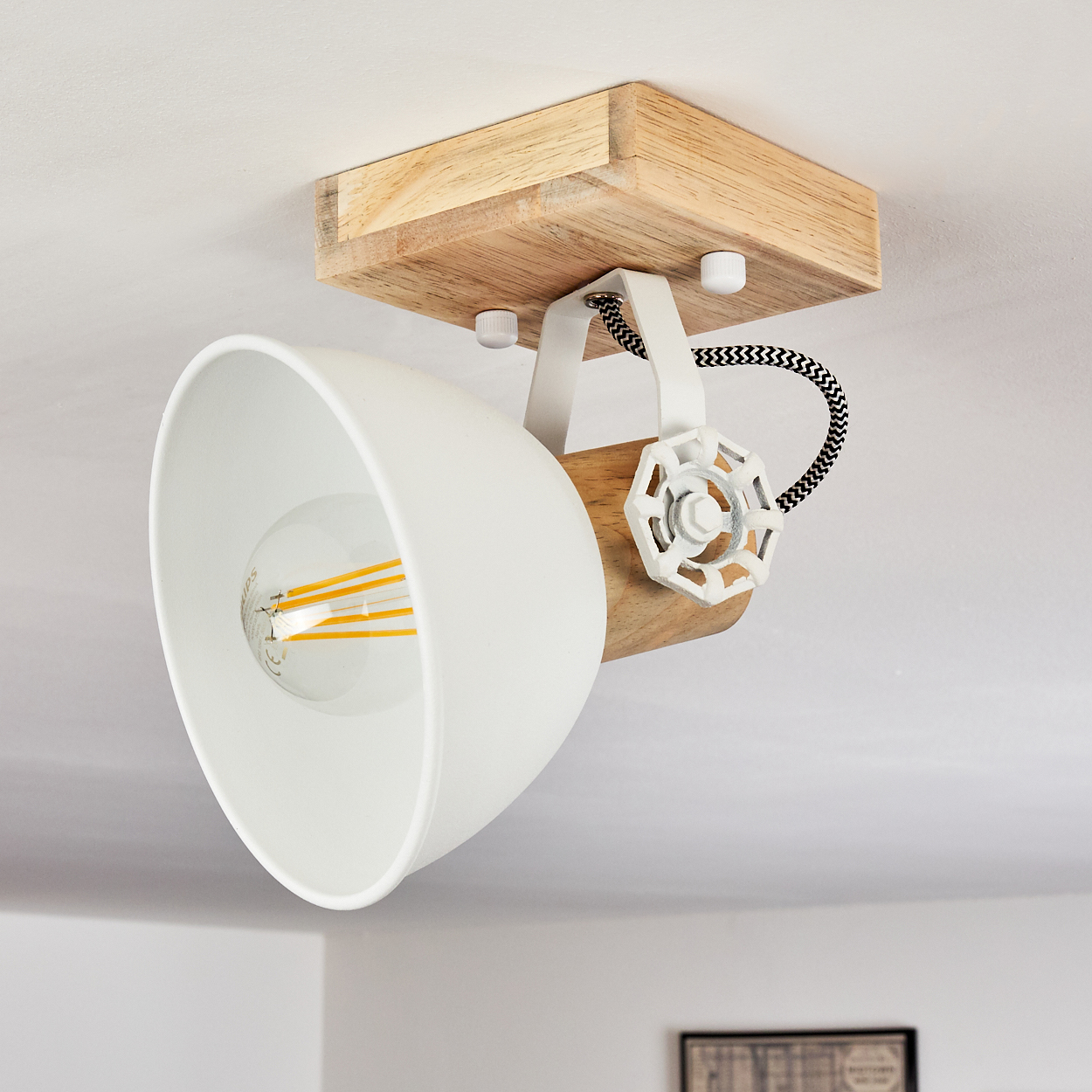 Eine weiße Lampe mit Holzfuß an der Decke. Sie hat eine Glühbirne.