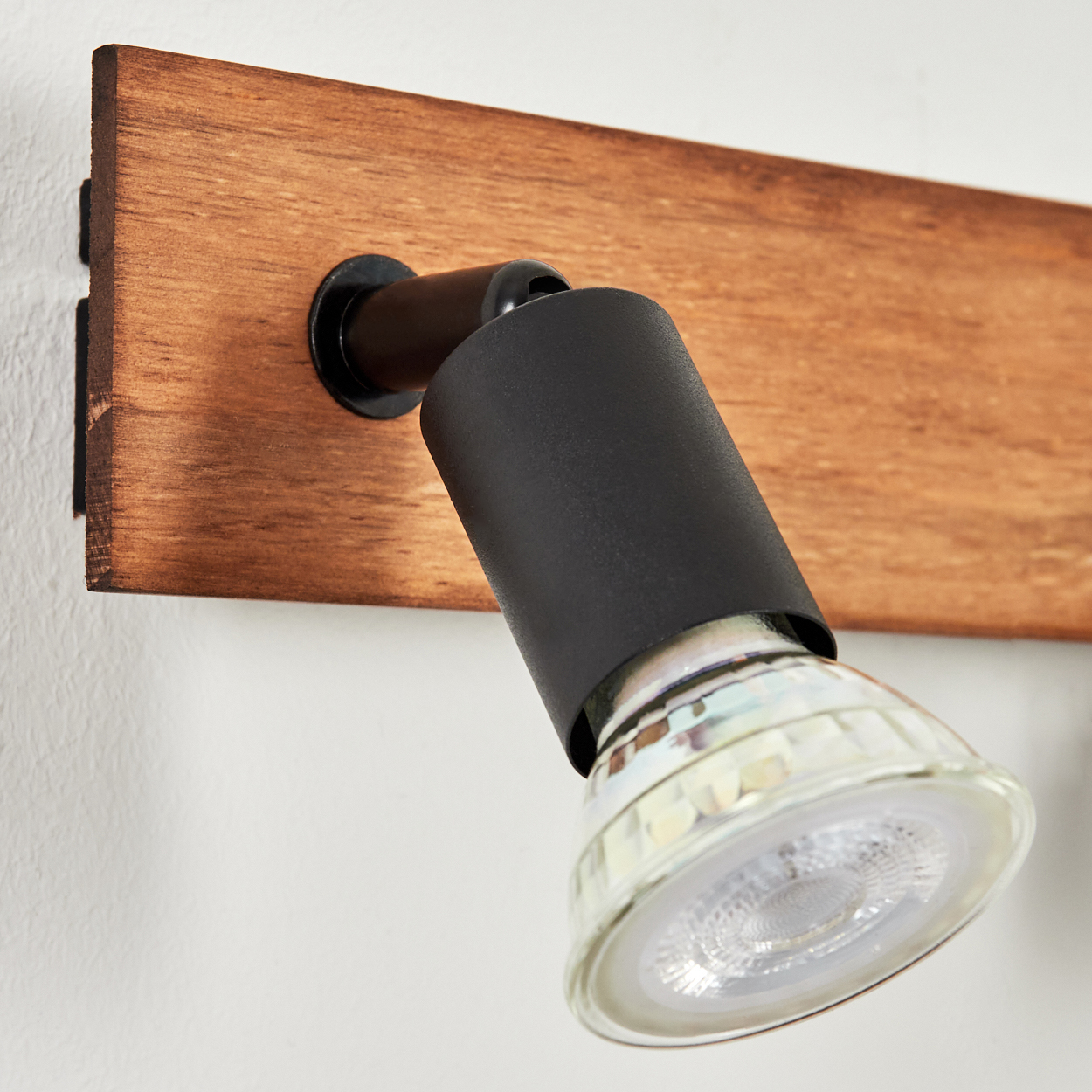 Ein schwarzer Strahler mit Holzbasis an einer weißen Wand.