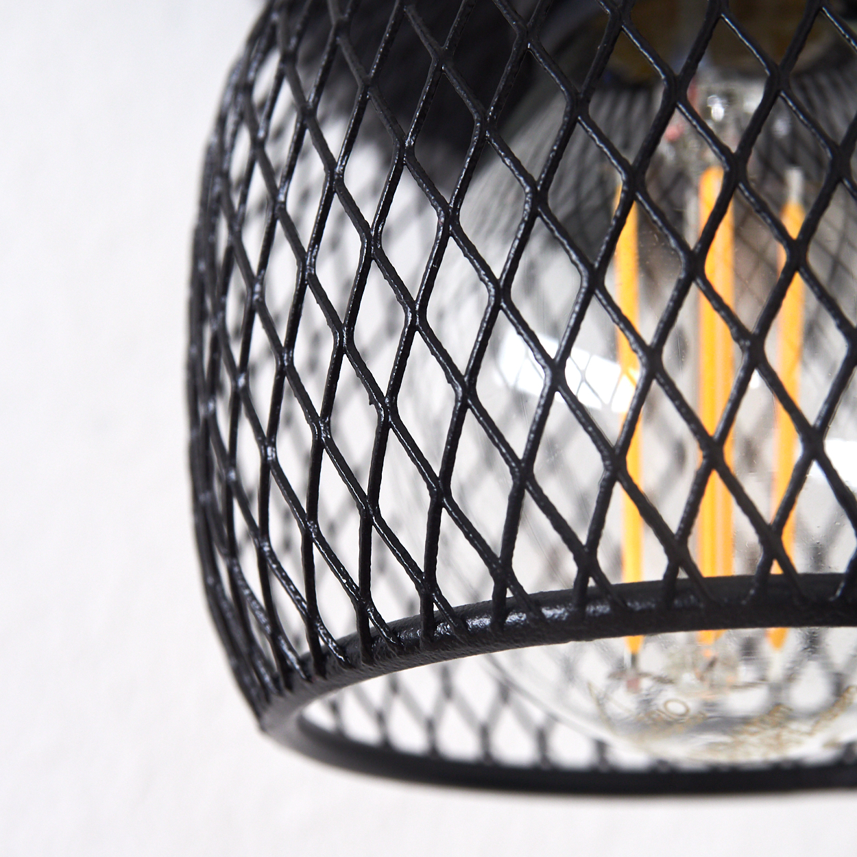 Eine Nahaufnahme einer schwarzen Drahtgitterlampe mit einer Glühbirne dahinter.