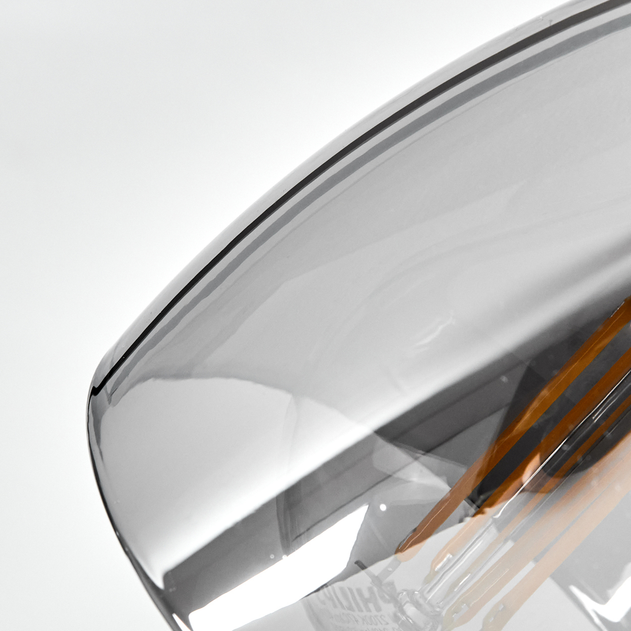 Eine Nahaufnahme einer Glühbirne mit transparentem, getöntem Glas und sichtbaren orangefarbenen Filamenten.