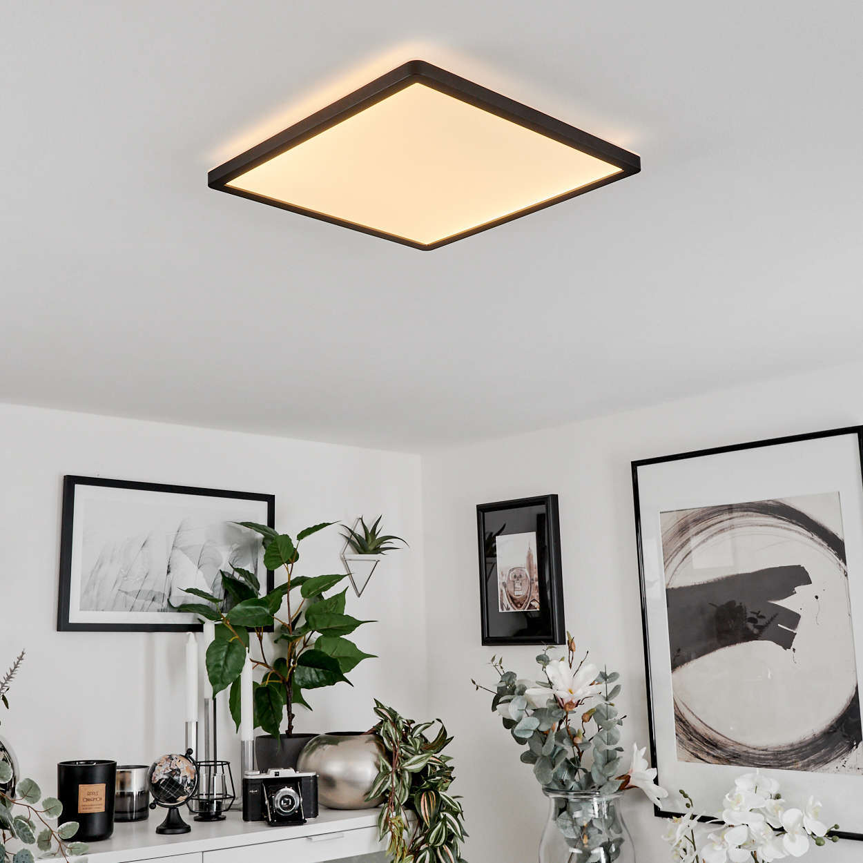 Ein moderner Deckenleuchter beleuchtet ein stilvolles Wohnzimmer mit Kunstwerken und Pflanzen.