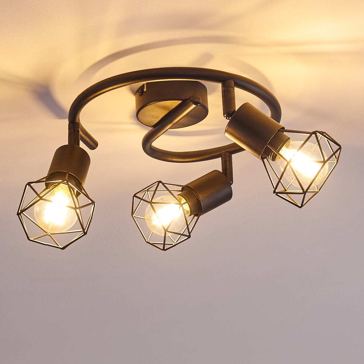 Dunkle Deckenleuchte mit drei verstellbaren Lampen und geometrischen Käfigschirmen.