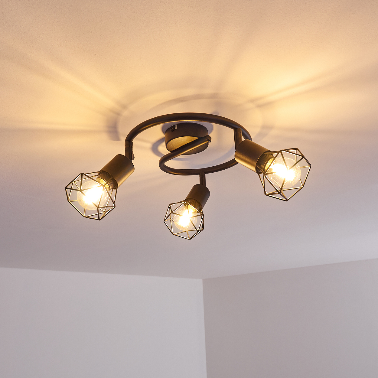 Eine Deckenleuchte mit drei Lampen in schwarzem Metall mit Drahtkäfigen.