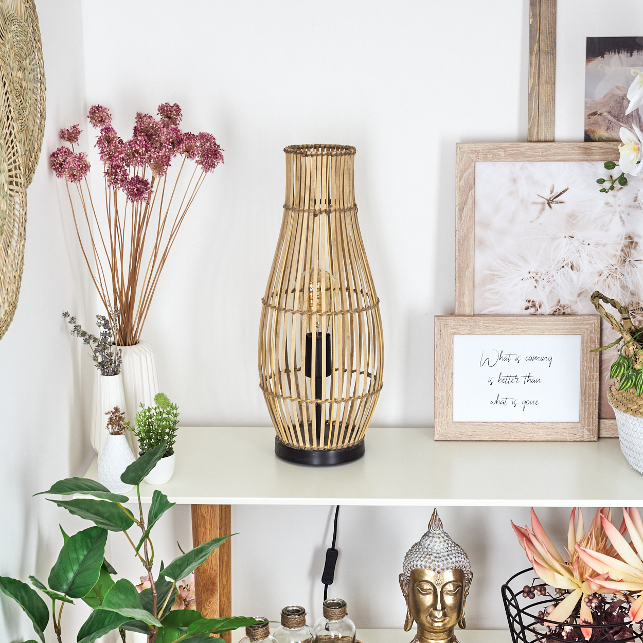 Ein dekoratives Regal mit einer Lampe aus Rattan, Trockenblumen und Bilderrahmen.