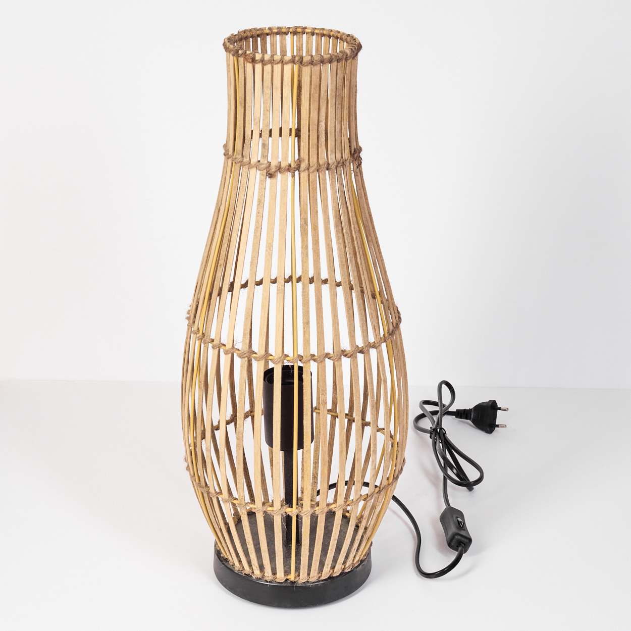 Eine hohe, bauchige Lampe aus Bambusstäben mit schwarzem Sockel und Kabel.