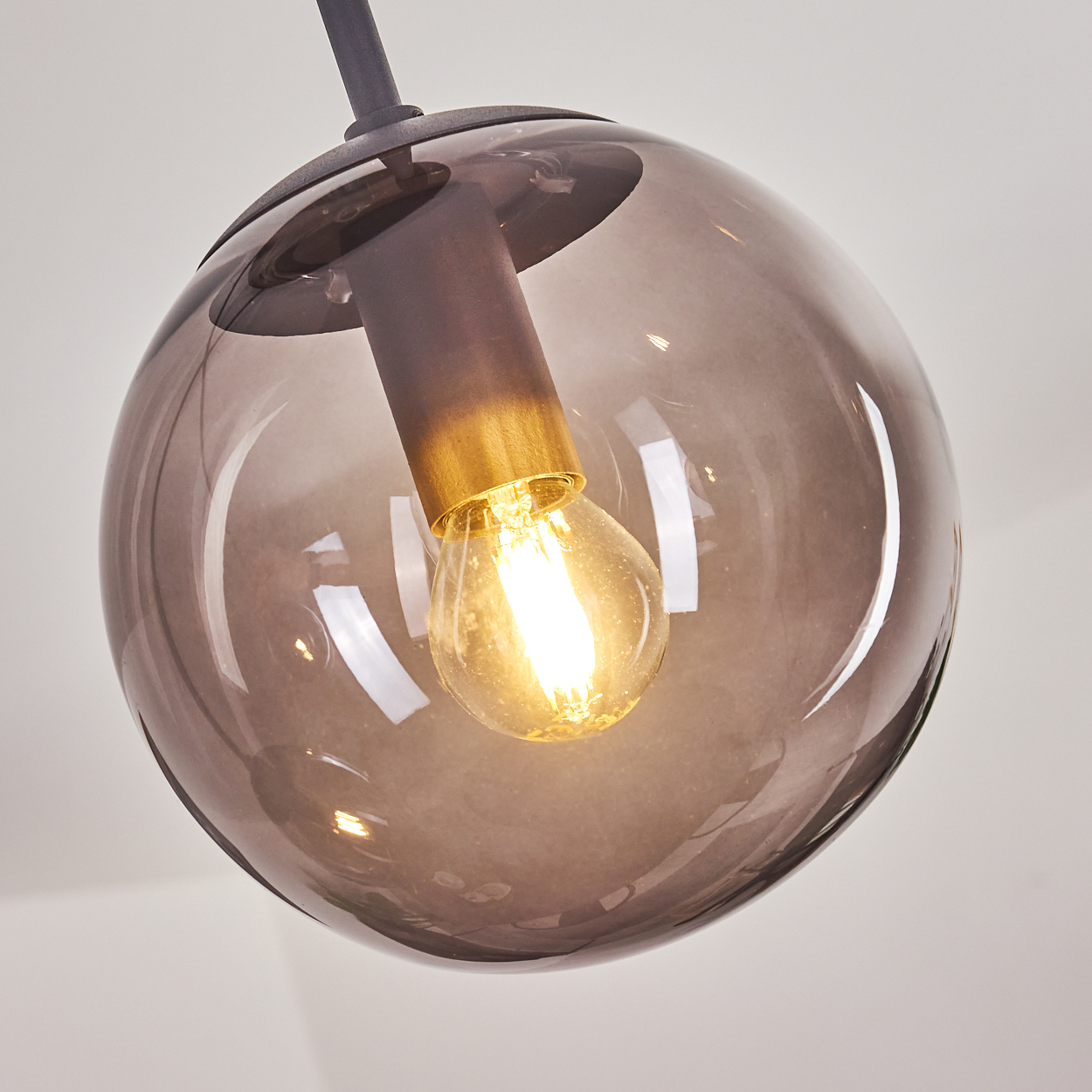 Eine rauchfarbene Glaskugel birgt eine Glühbirne mit goldenem Sockel.