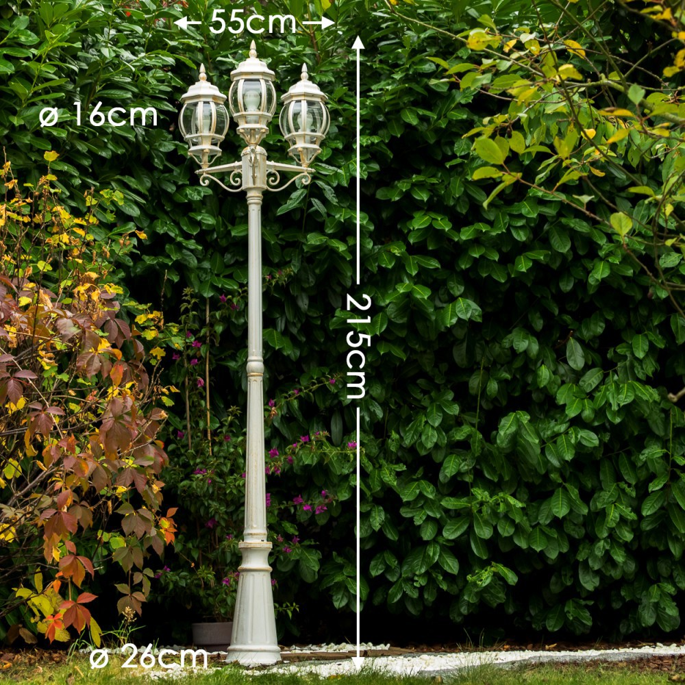 Eine weiße dreiflammige Laterne auf einem Sockel, 215cm hoch, vor üppigem Grün.