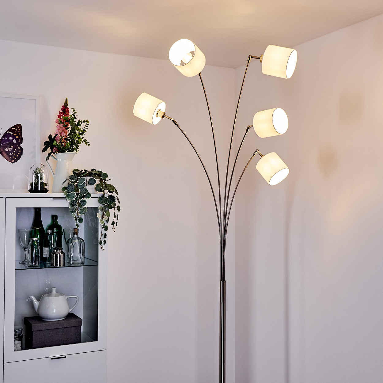 Bogenlampe mit fünf Lichtern neben einem weißen Schrank mit Dekorationen.
