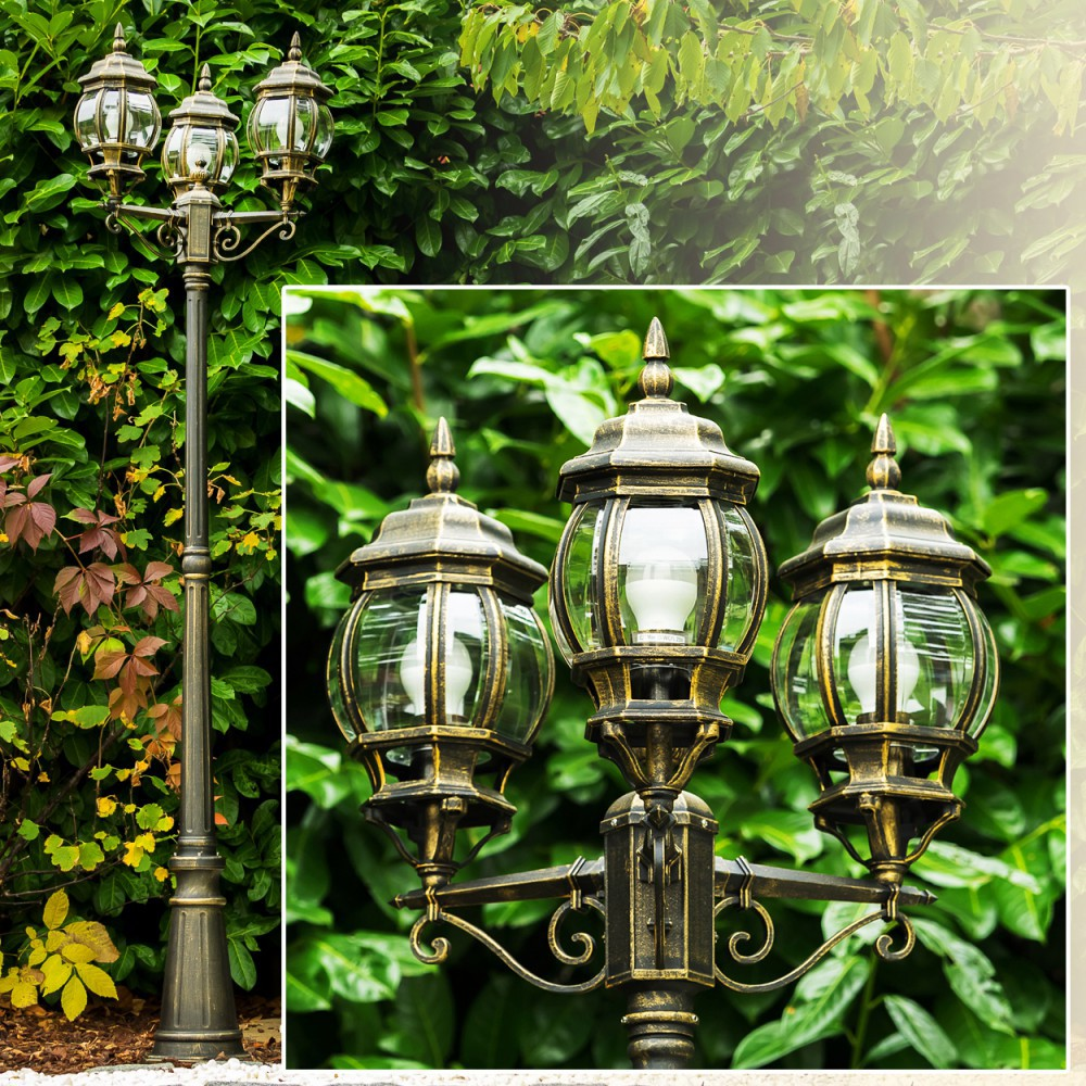 Eine schmiedeeiserne Lampe mit drei Glaskugelleuchten vor grünem Laub.