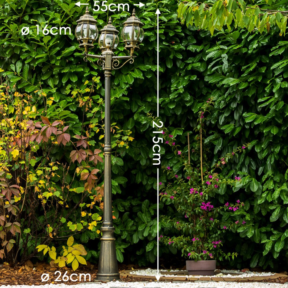 Eine antike gusseiserne Stehleuchte mit drei Lampen steht vor einer grünen Hecke.