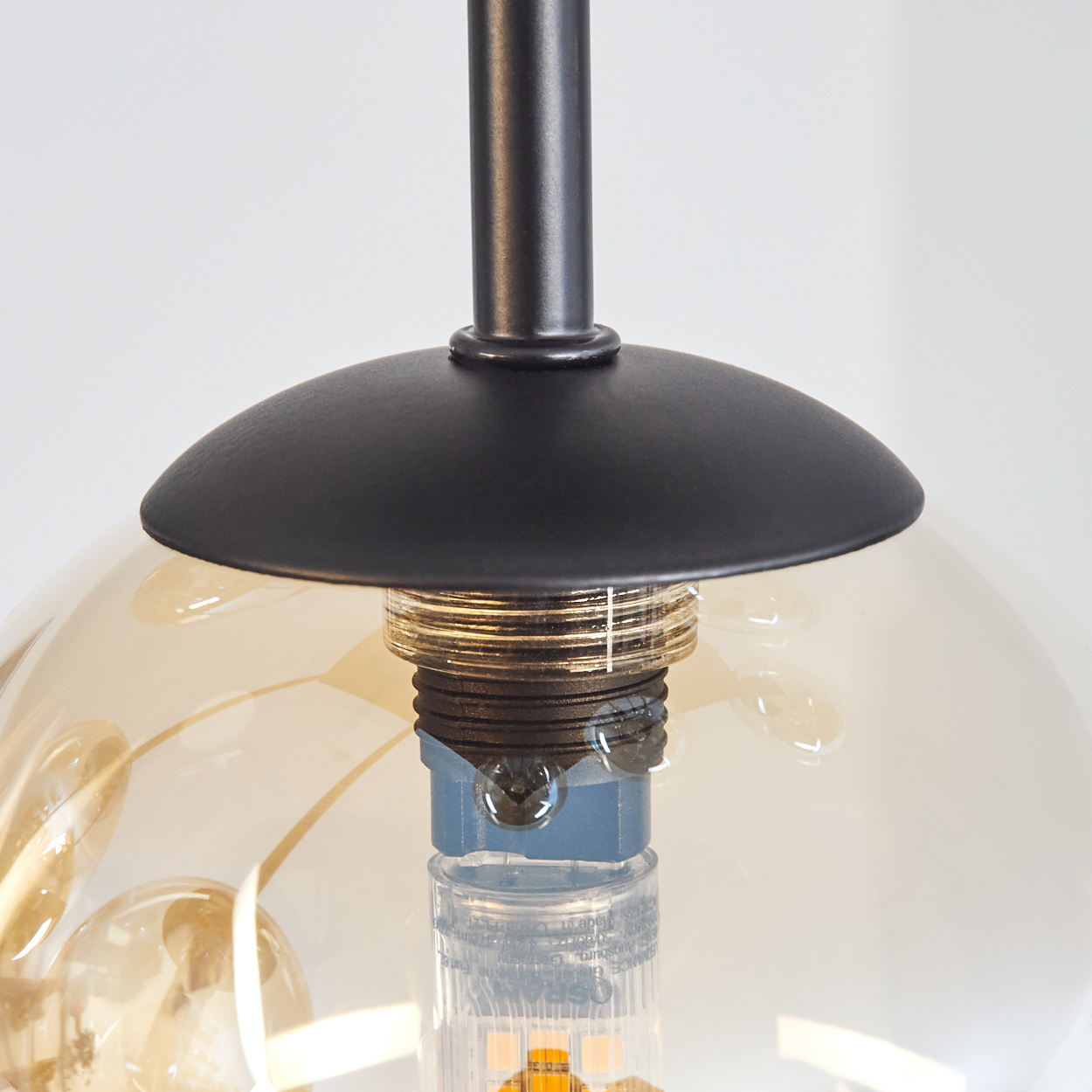 Nahaufnahme einer Pendelleuchte mit bernsteinfarbenem Glas und schwarzer Metallhalterung.