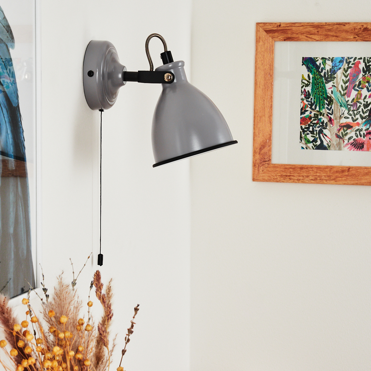 Graue Wandlampe mit Zugschalter neben einem Bild mit Vögeln.