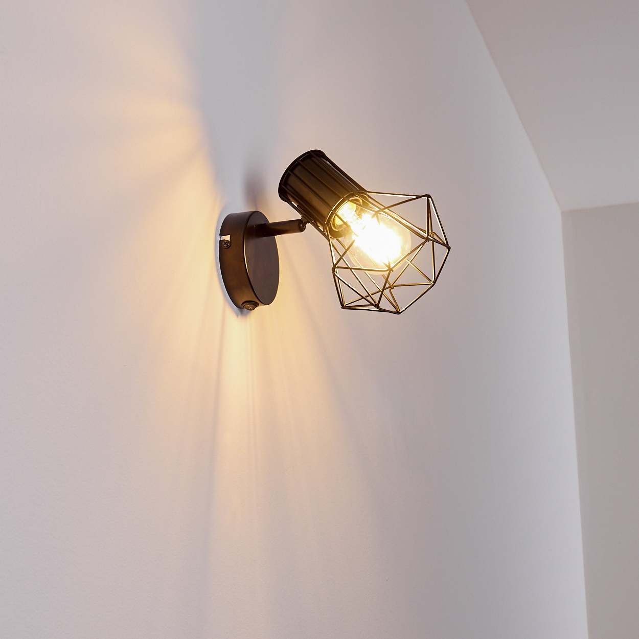 Eine Wandleuchte mit schwarzem Metallkäfig und sichtbarem Glühfaden leuchtet hell.