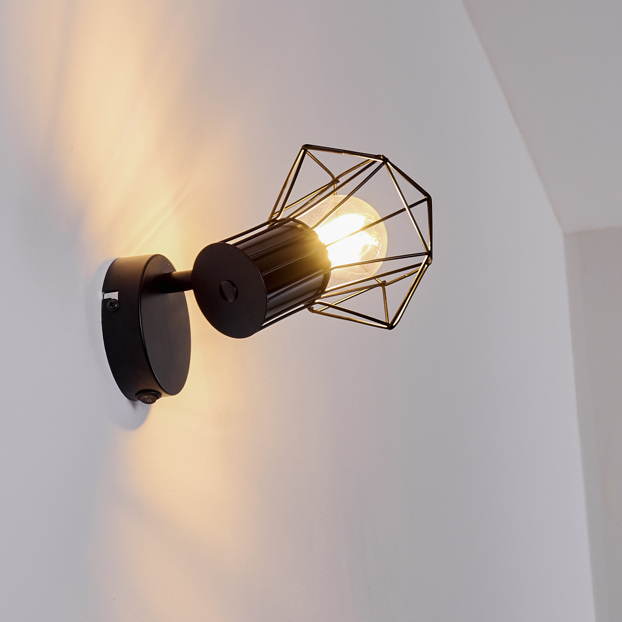 Ein schwarzer Wandspot mit einem geometrischen Drahtkäfig und sichtbarer Glühbirne.