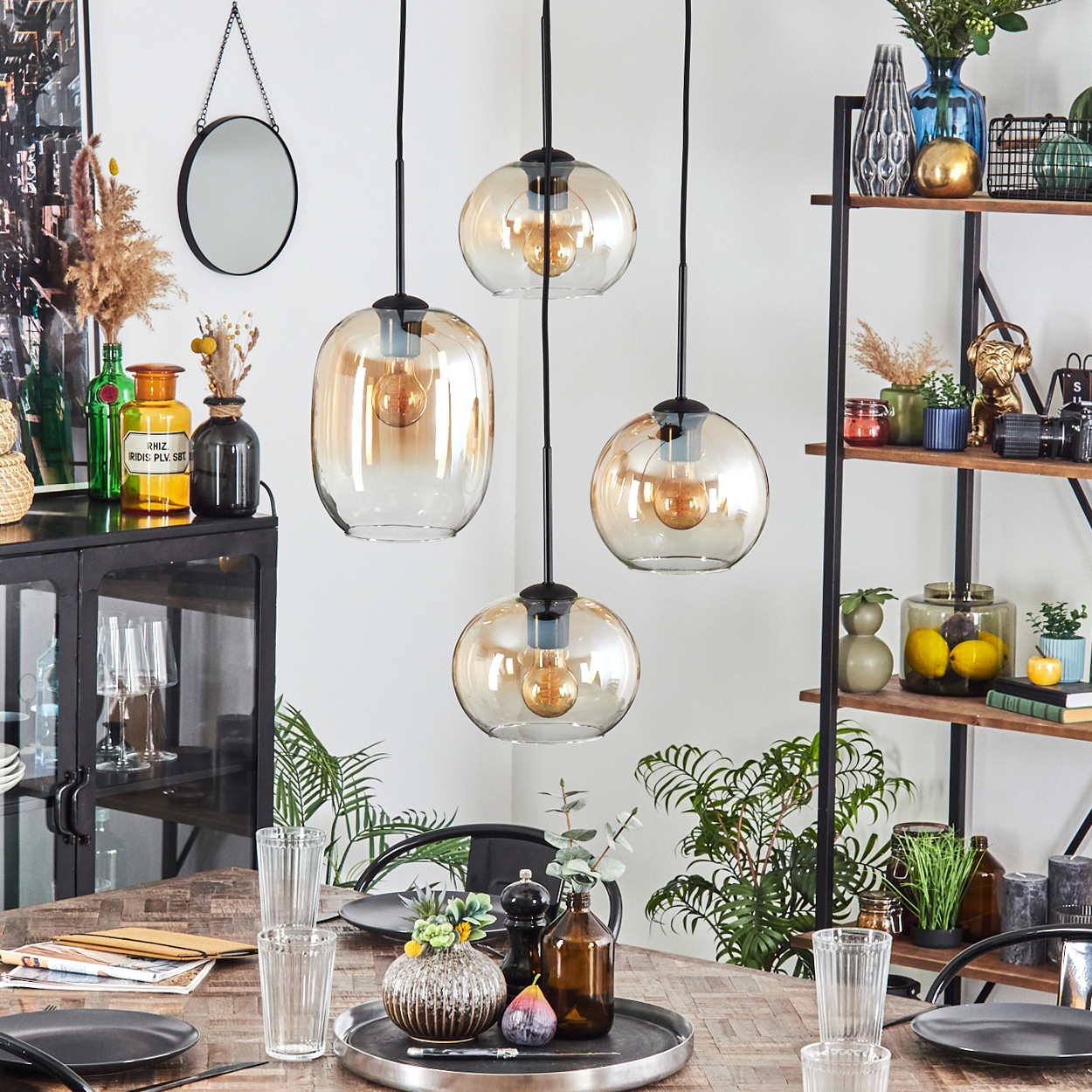 Ein Esstisch mit Gläsern, Tellern und Dekoration. Hängende Lampen darüber.