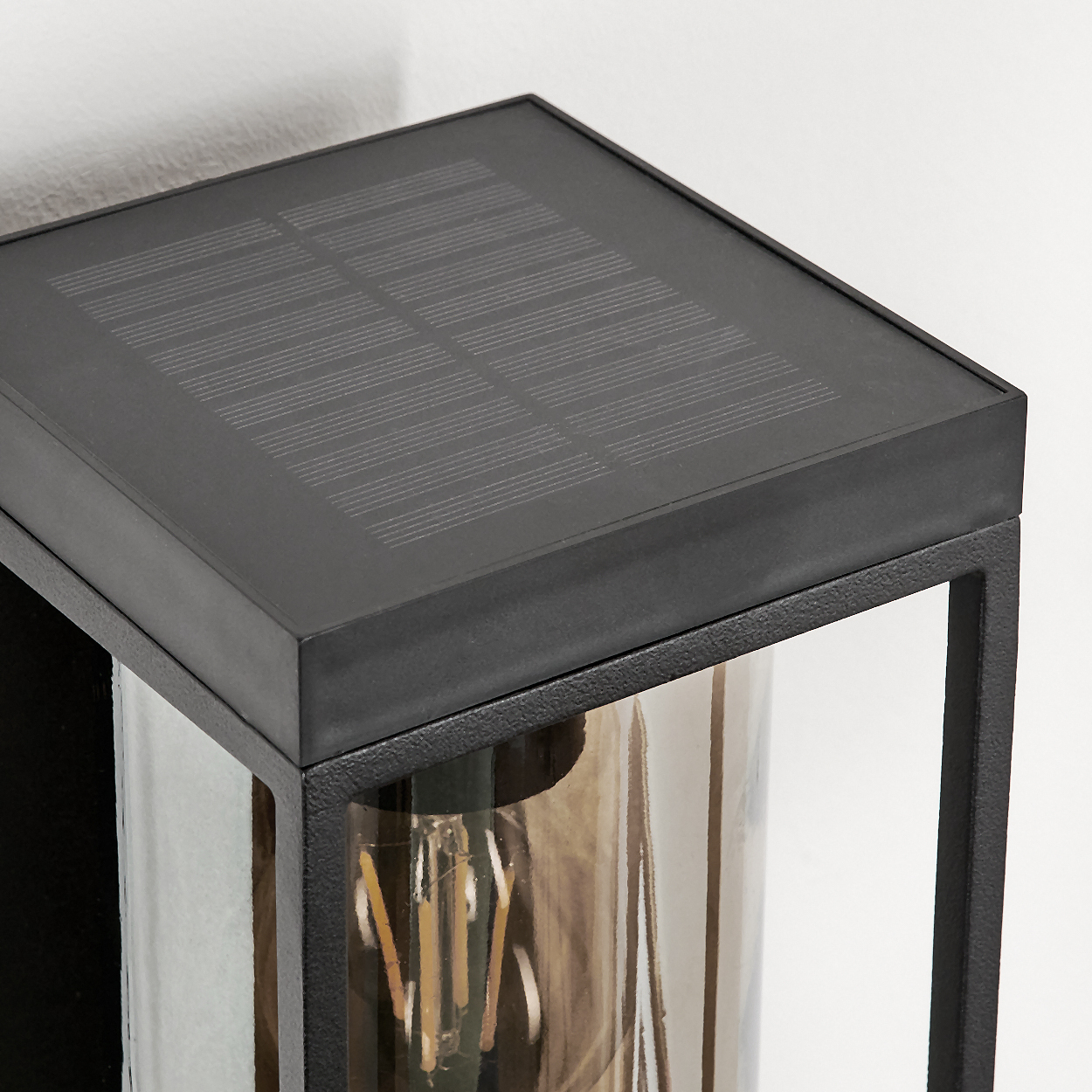 Schwarze Wandleuchte mit Solarmodul und Glühbirne im Glaszylinder.