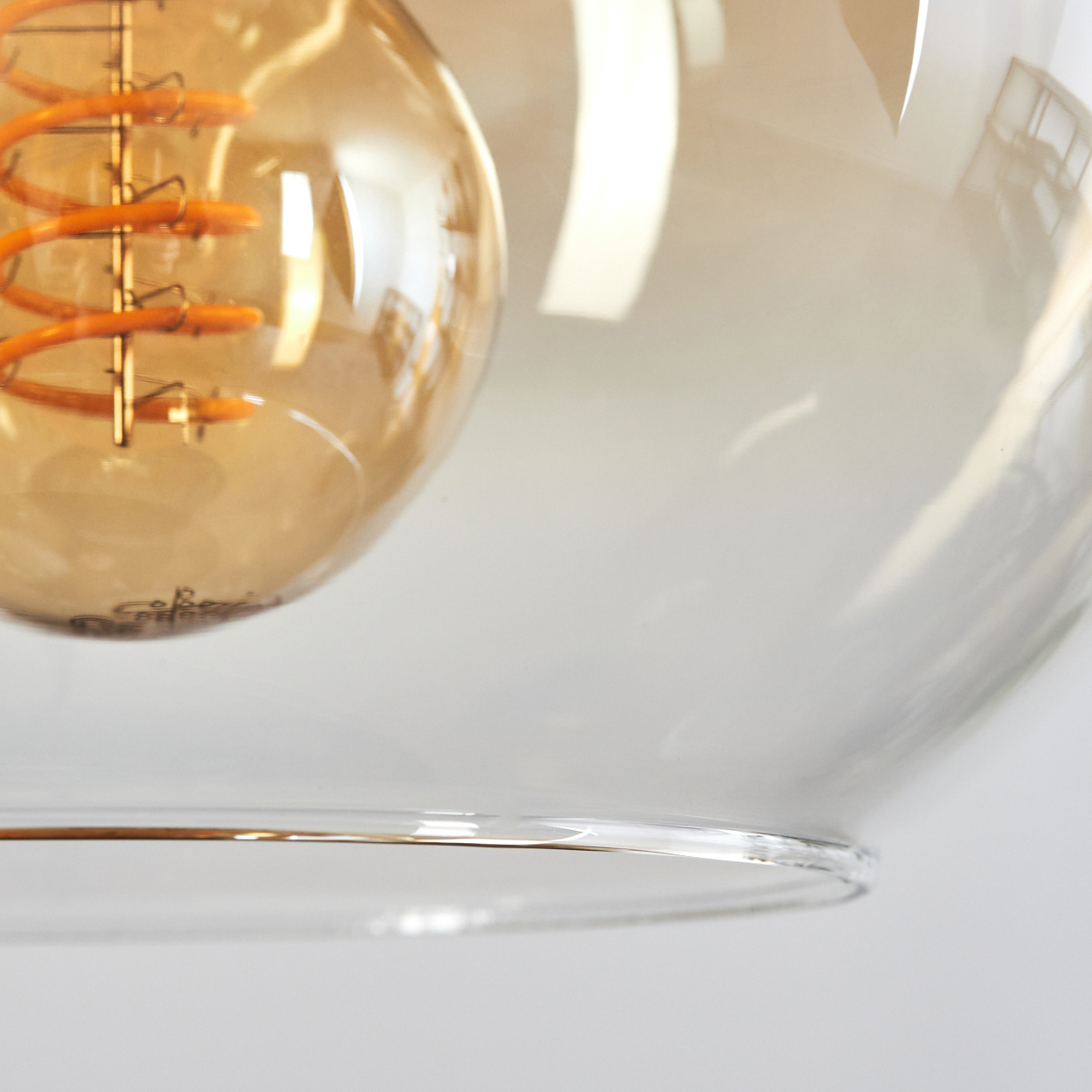 Nahaufnahme einer bernsteinfarbenen Glühbirne mit Spiralwendel in einem Glaslampenschirm.