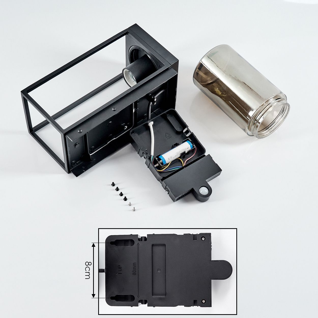 Ein zerlegter Laternenbausatz mit schwarzem Metallrahmen, Glaszylinder, Batterie und Schrauben.