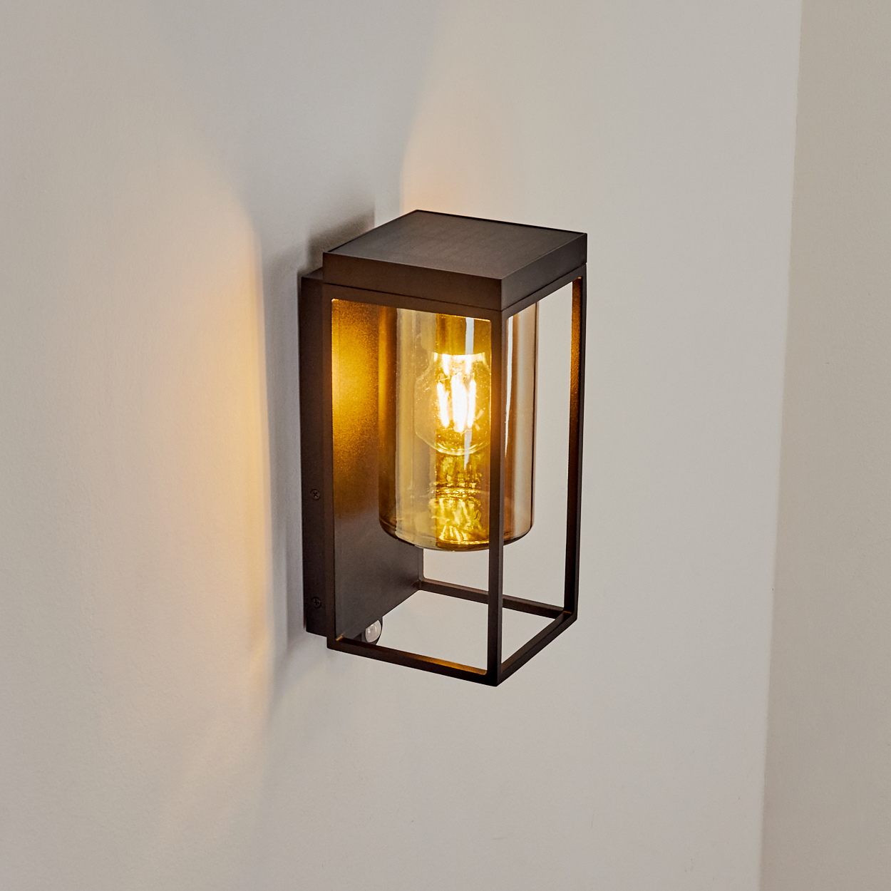 Eine dunkle Wandleuchte mit einem zylindrischen Bernstein-Glas und sichtbarer Glühbirne.