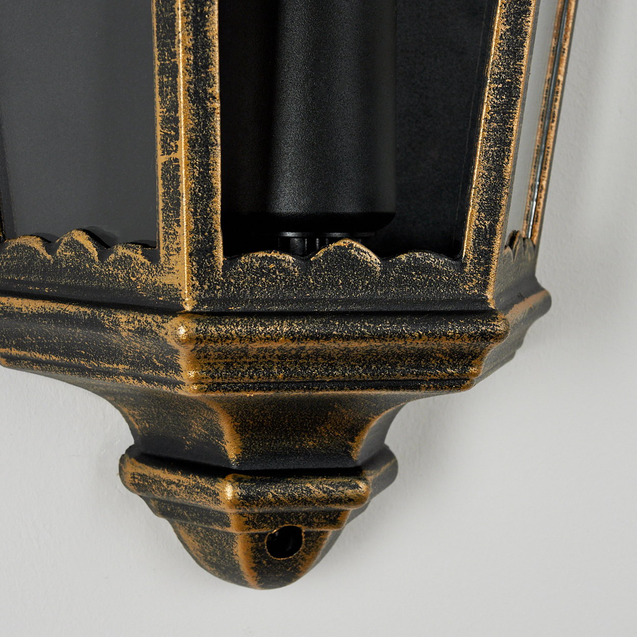 Nahaufnahme einer verzierten schwarzen und goldenen Wandleuchte mit einem schwarzen Zylinder.