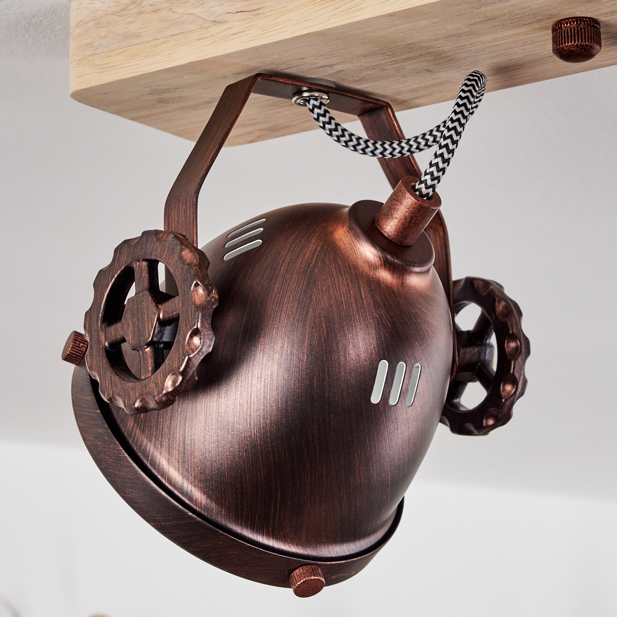 Eine bronzefarbene Lampe mit Zahnrad-Akzenten, befestigt an einem Holzbalken.