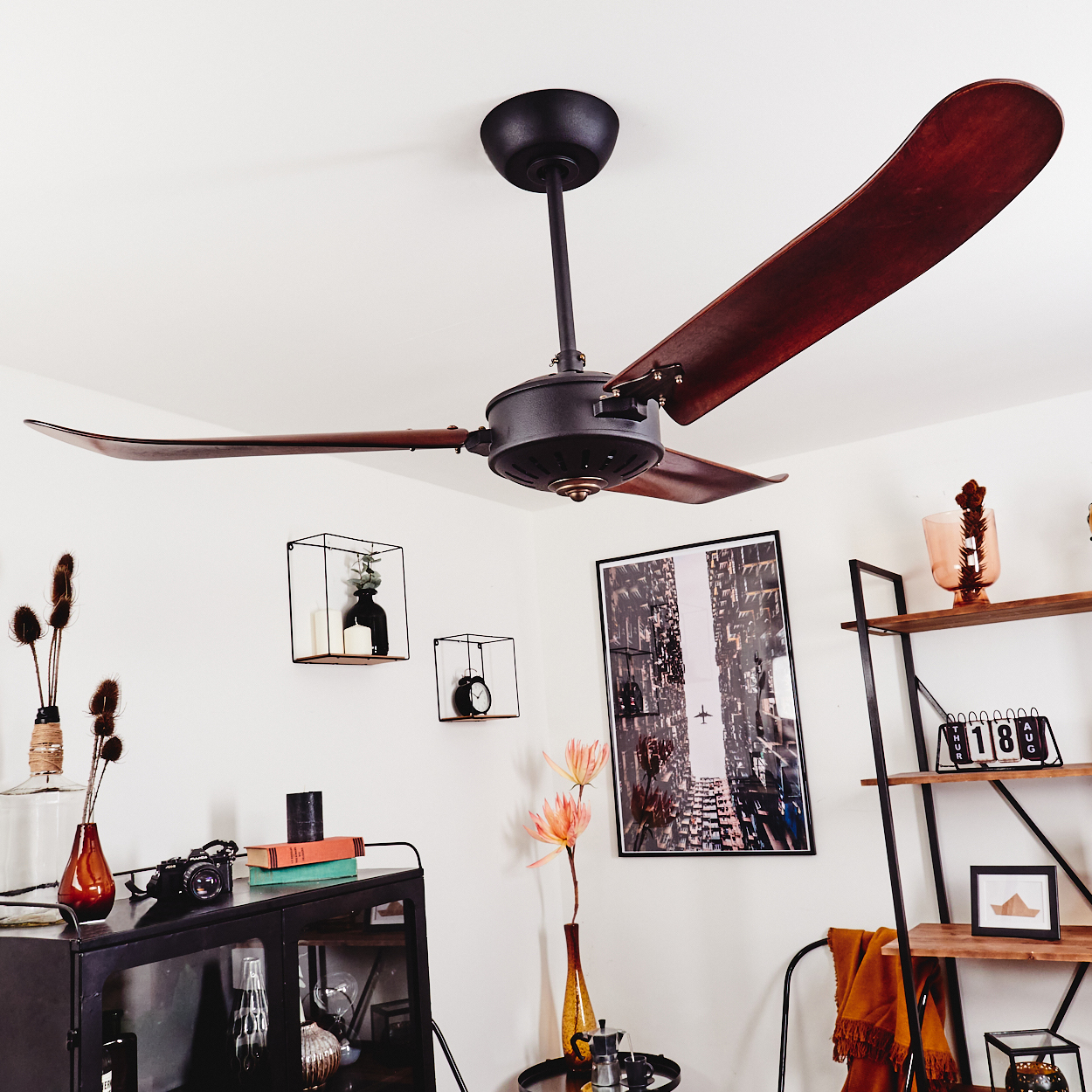 Eine Deckenventilator mit Holzblättern über einem schwarzen Schrank mit Dekor.