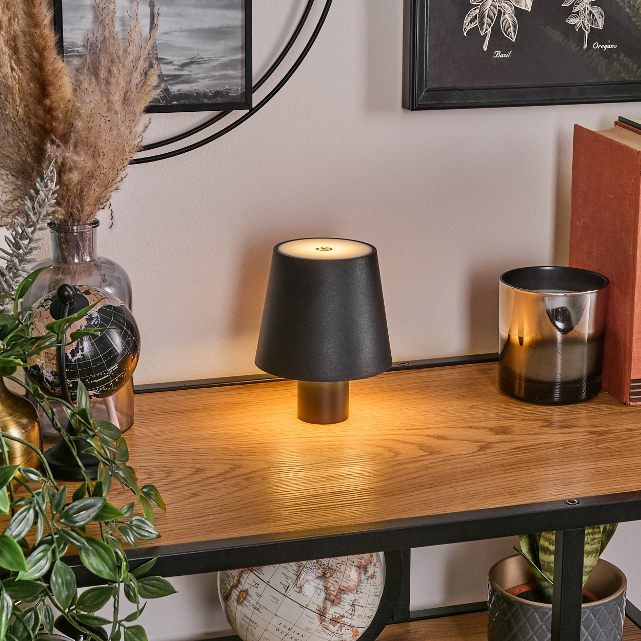 Eine schwarze Lampe leuchtet auf einem Holztisch neben einem Globus und Büchern.