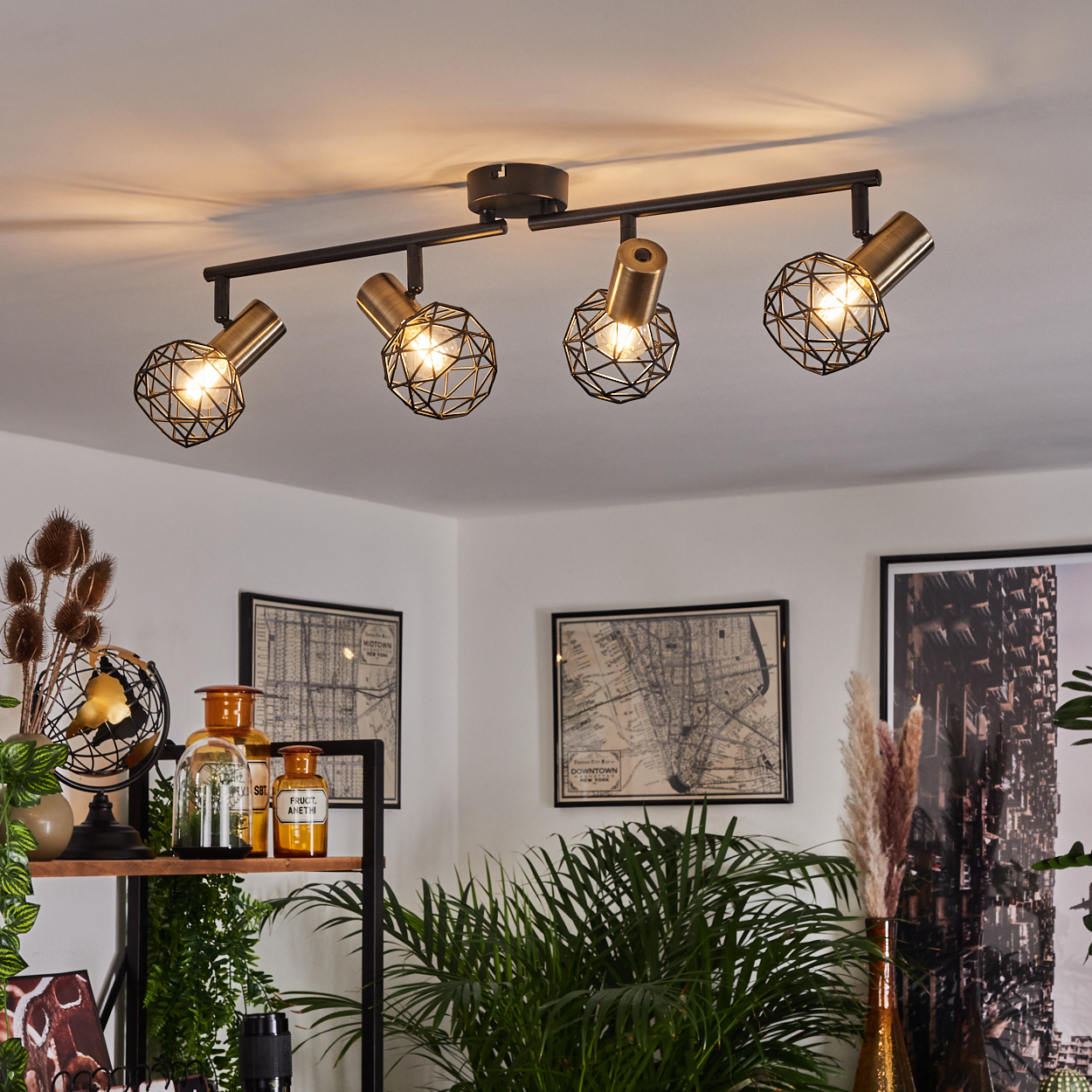 Eine moderne schwarze Schienenleuchte mit vier Messinglampen im Käfigstil hängt von einer weißen Decke.