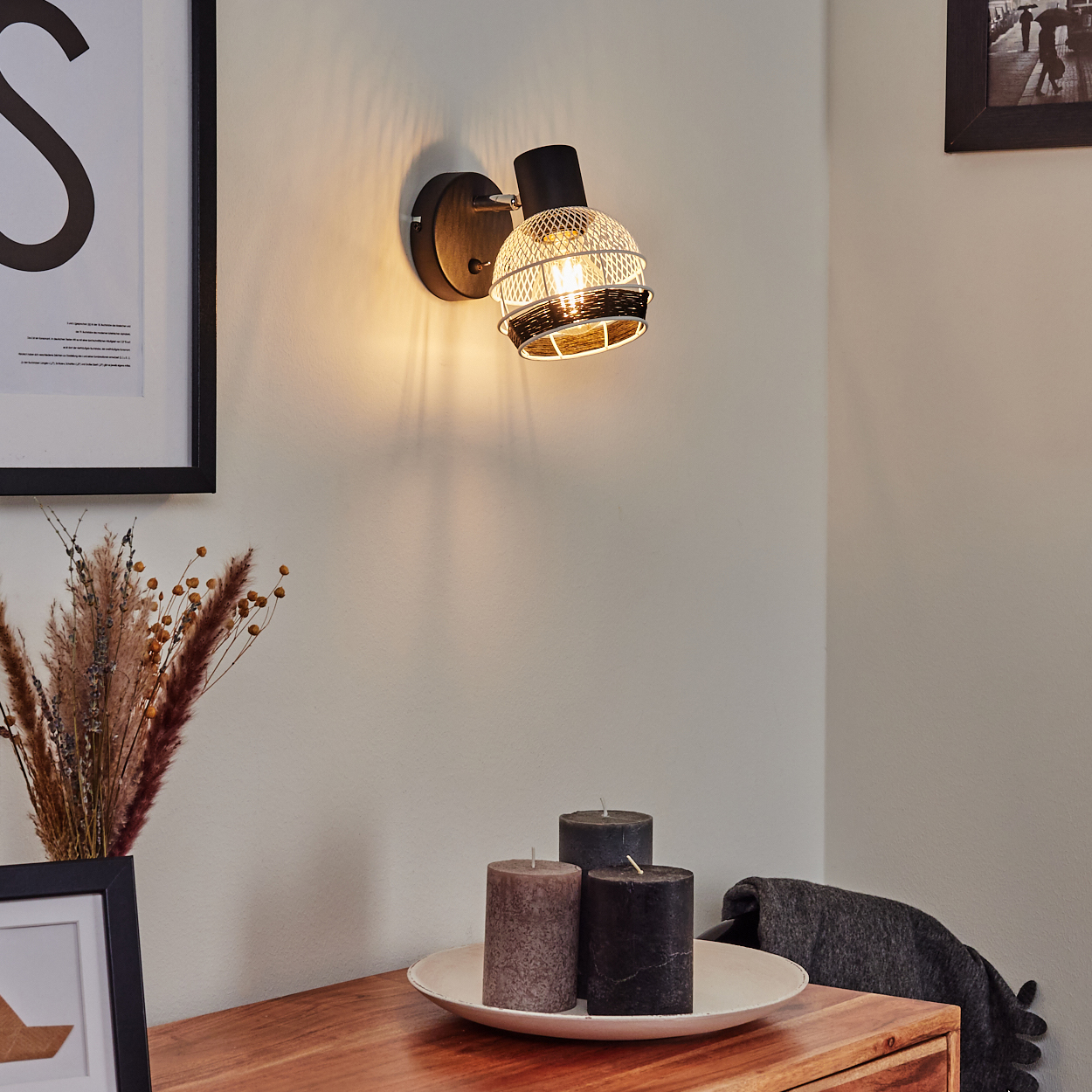 Eine Wandleuchte mit Drahtschirm über einem Holztisch mit Kerzen.