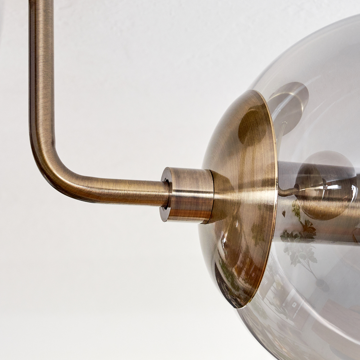 Messingarmatur mit Rauchglas-Lampenschirm und sichtbaren Glühbirnen vor weißem Hintergrund.