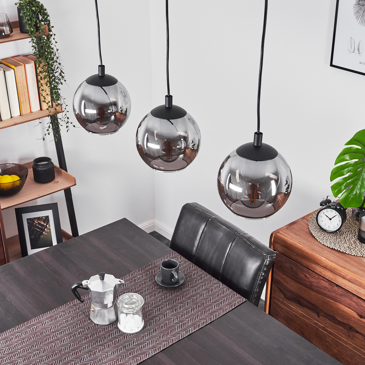 Drei kugelförmige Hängelampen über einem dunklen Holztisch mit Kaffeekanne.