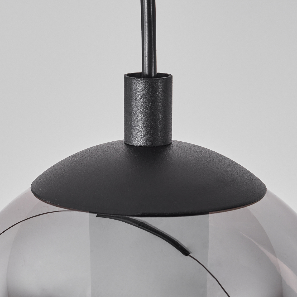 Nahaufnahme einer schwarzen Pendelleuchte mit einem schwarzen Metallschirm und einem Glaslampenschirm.