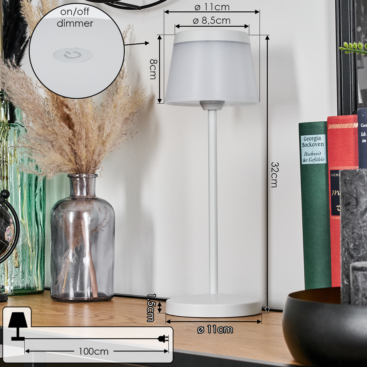 Eine weiße Tischlampe mit Maßen steht auf einem Regal neben Büchern und einem Glas.