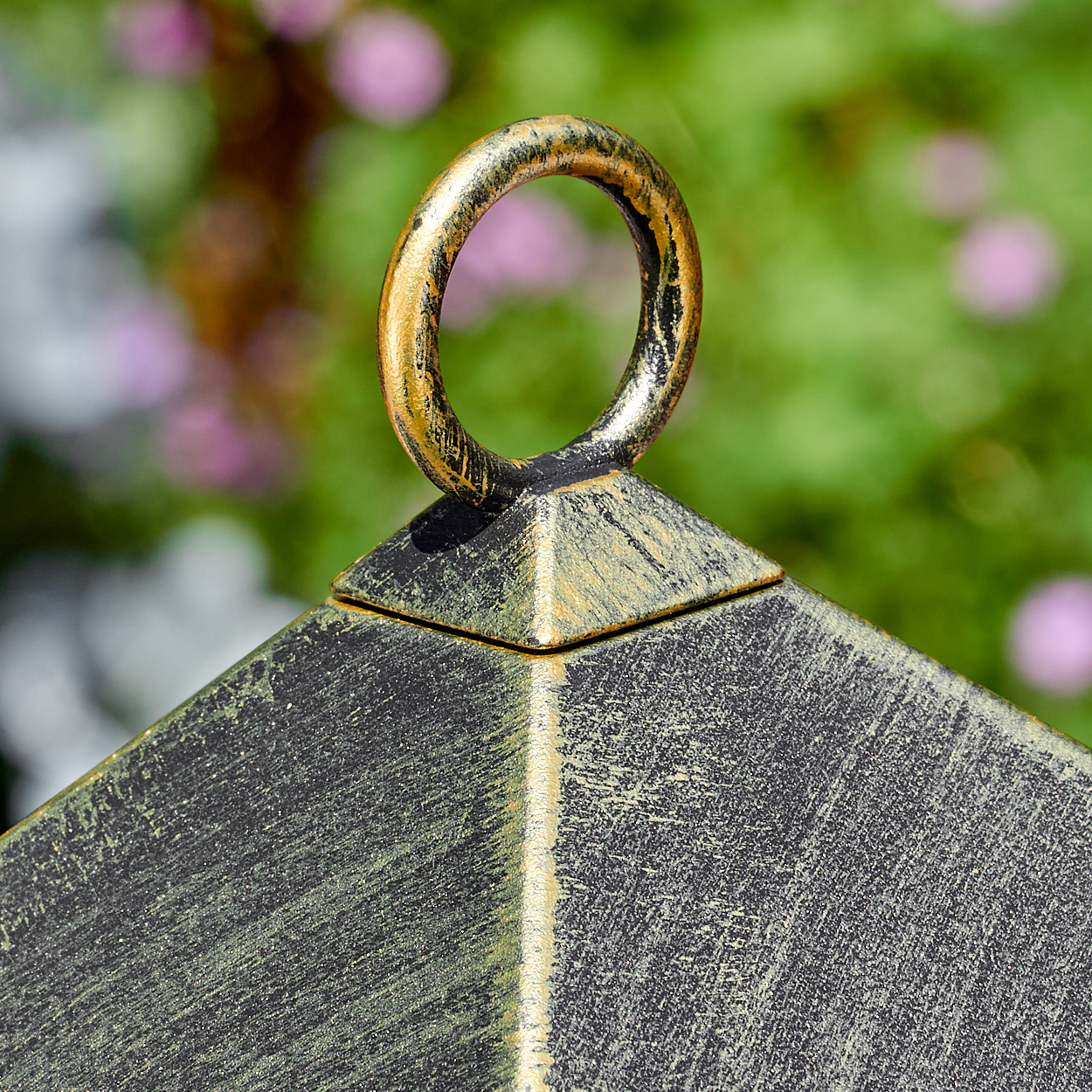 Nahaufnahme einer dunklen Laternenoberseite mit goldenem Ring, grüner Hintergrund.