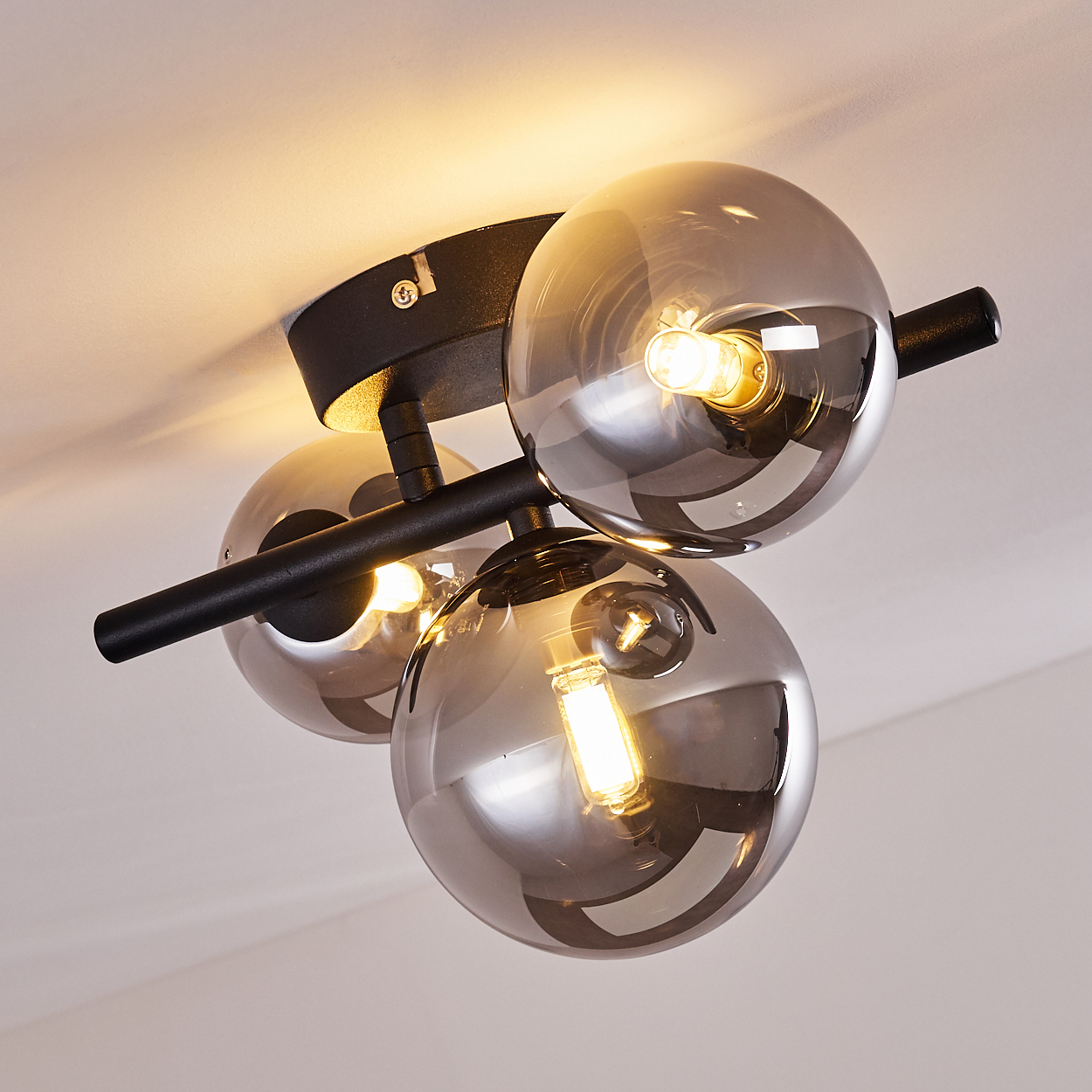 Deckenleuchte mit drei rauchglasfarbenen Kugeln und schwarzen Metallarmen.