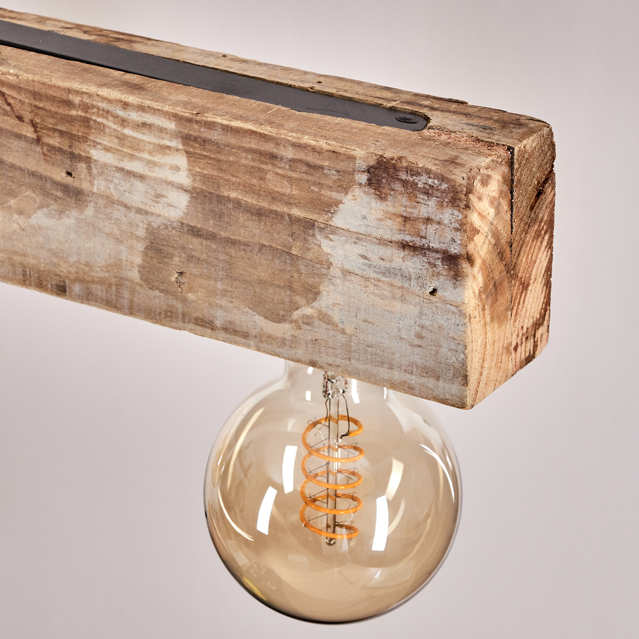 Eine Glühbirne mit sichtbarem Glühfaden hängt unter einem Holzbalken.