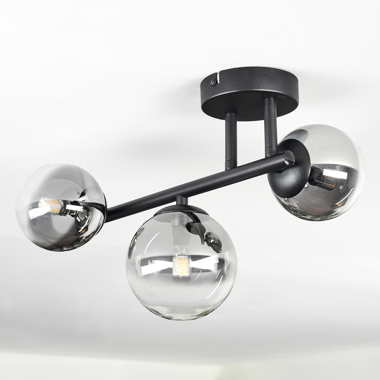 Schwarzer Deckenleuchter mit drei Rauchglas-Kugeln und sichtbaren LED-Lampen.