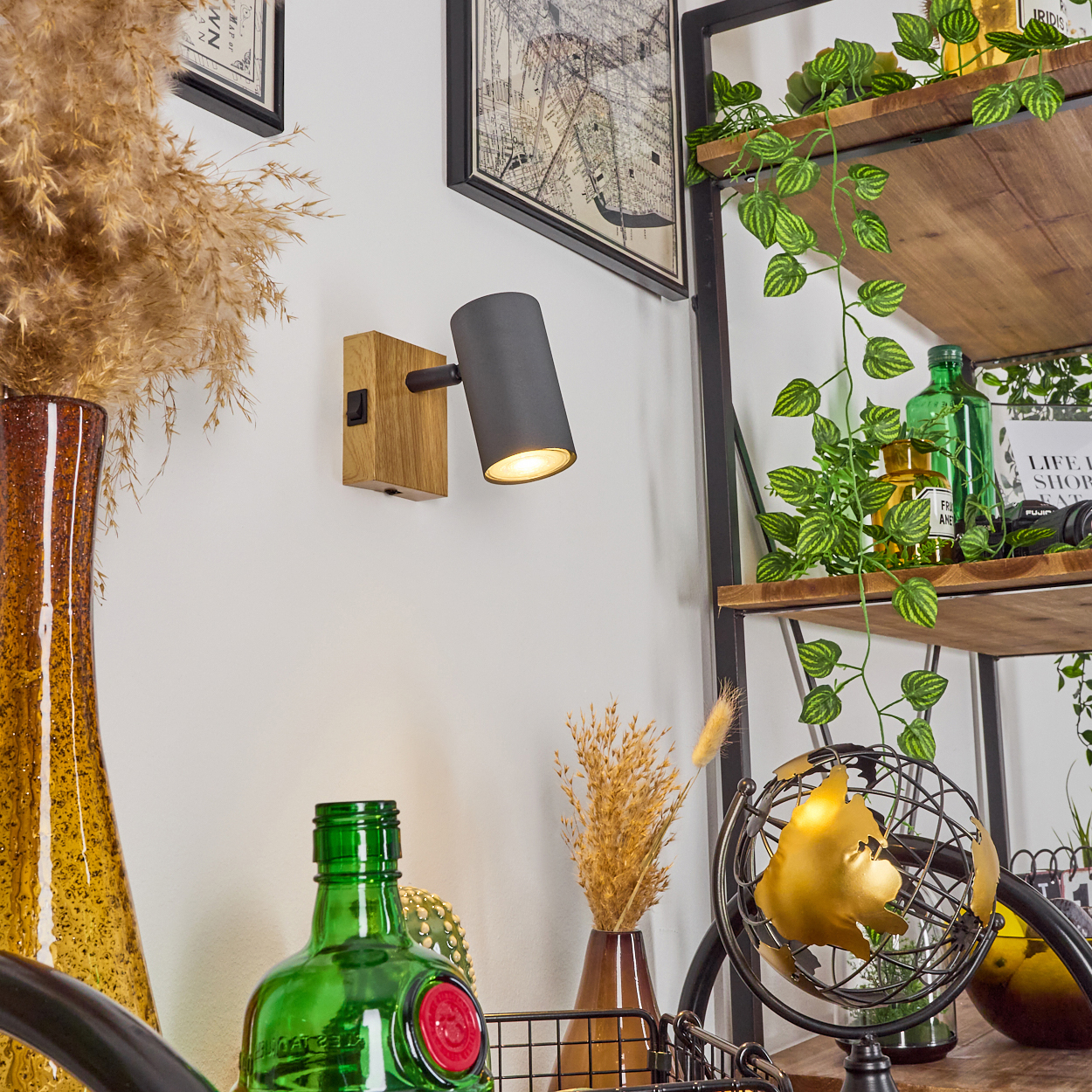 Ein Wandstrahler mit Holzsockel beleuchtet eine weiße Wand neben einem hohen Glasgefäß.
