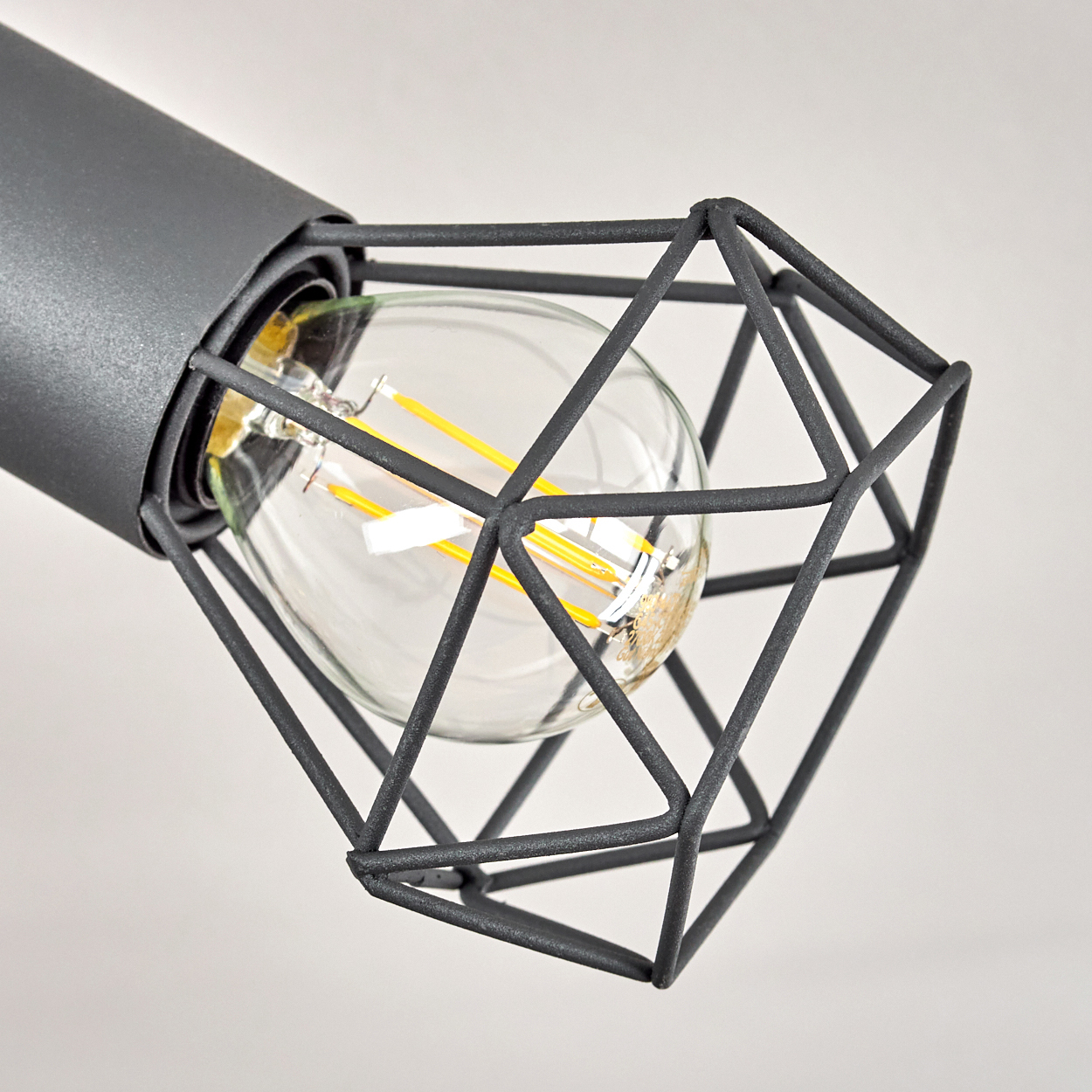 Graue Lampe mit Glühbirne und geometrischem Drahtkäfig.