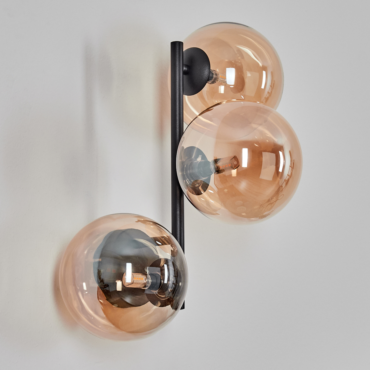Eine moderne Lampe mit drei bernsteinfarbenen Glaskugeln an einem schwarzen vertikalen Stab.