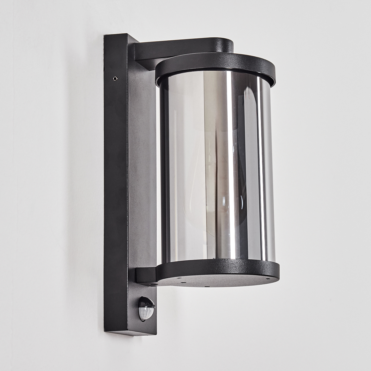 Eine schwarze Wandlampe mit zylindrischem Glas und Bewegungssensor.