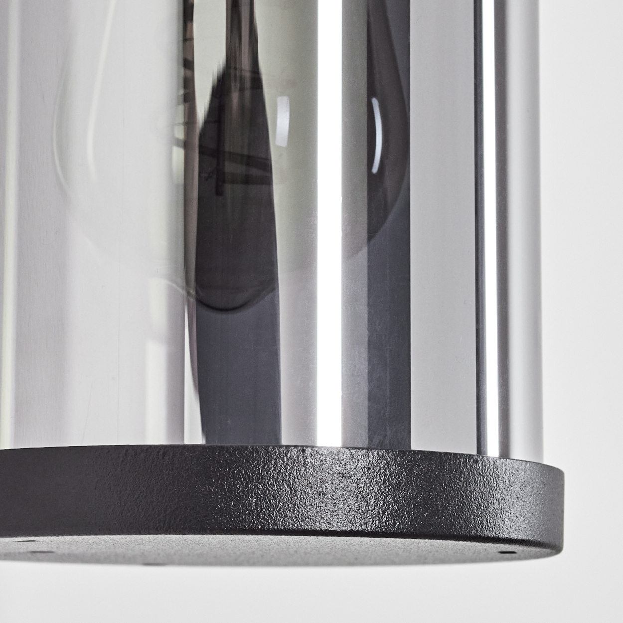 Nahaufnahme des unteren Teils einer Zylinderlampe mit schwarzem Sockel und Glas.
