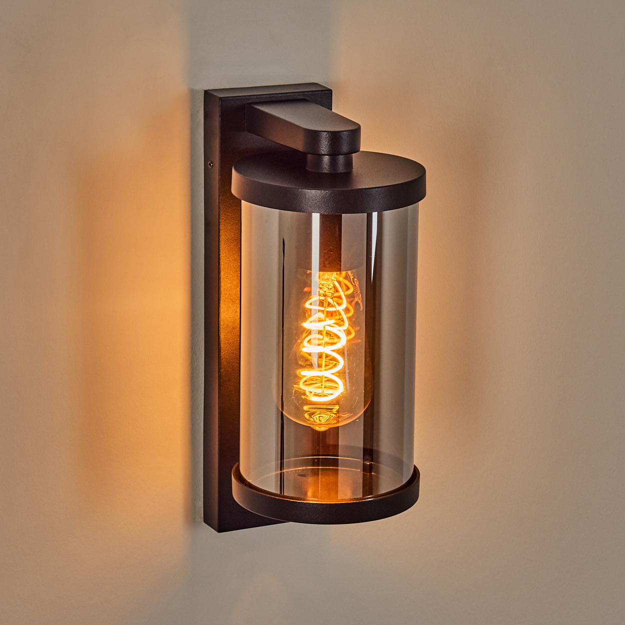 Ein schwarzer Wandleuchter mit einem zylindrischen Glas und einer Edison-Glühbirne.