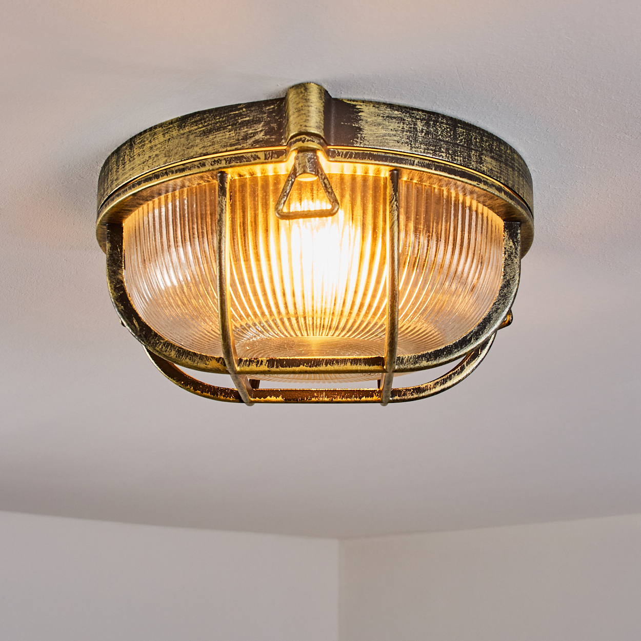 Eine antike, goldfarbene Deckenleuchte mit geripptem Glas und Metallschutzgitter.